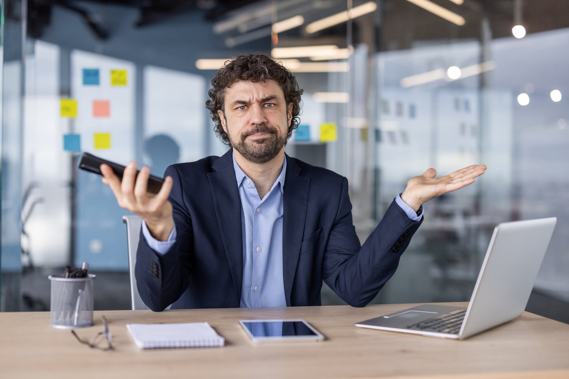 Operations manager at a desk in a modern office looking at a laptop and phone while surrounded by disconnected systems and manual processes