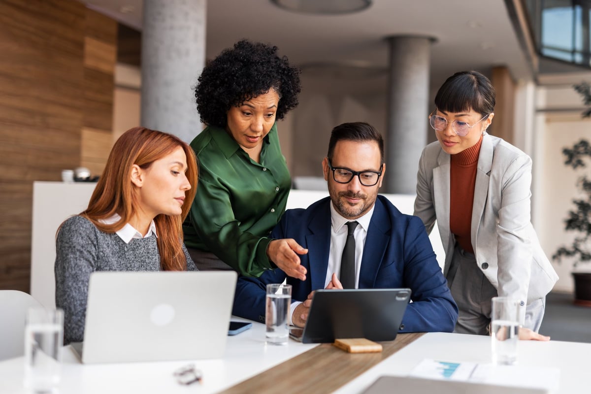 Professionals collaborate in a modern office environment with laptops and tablets, fostering teamwork and productivity.