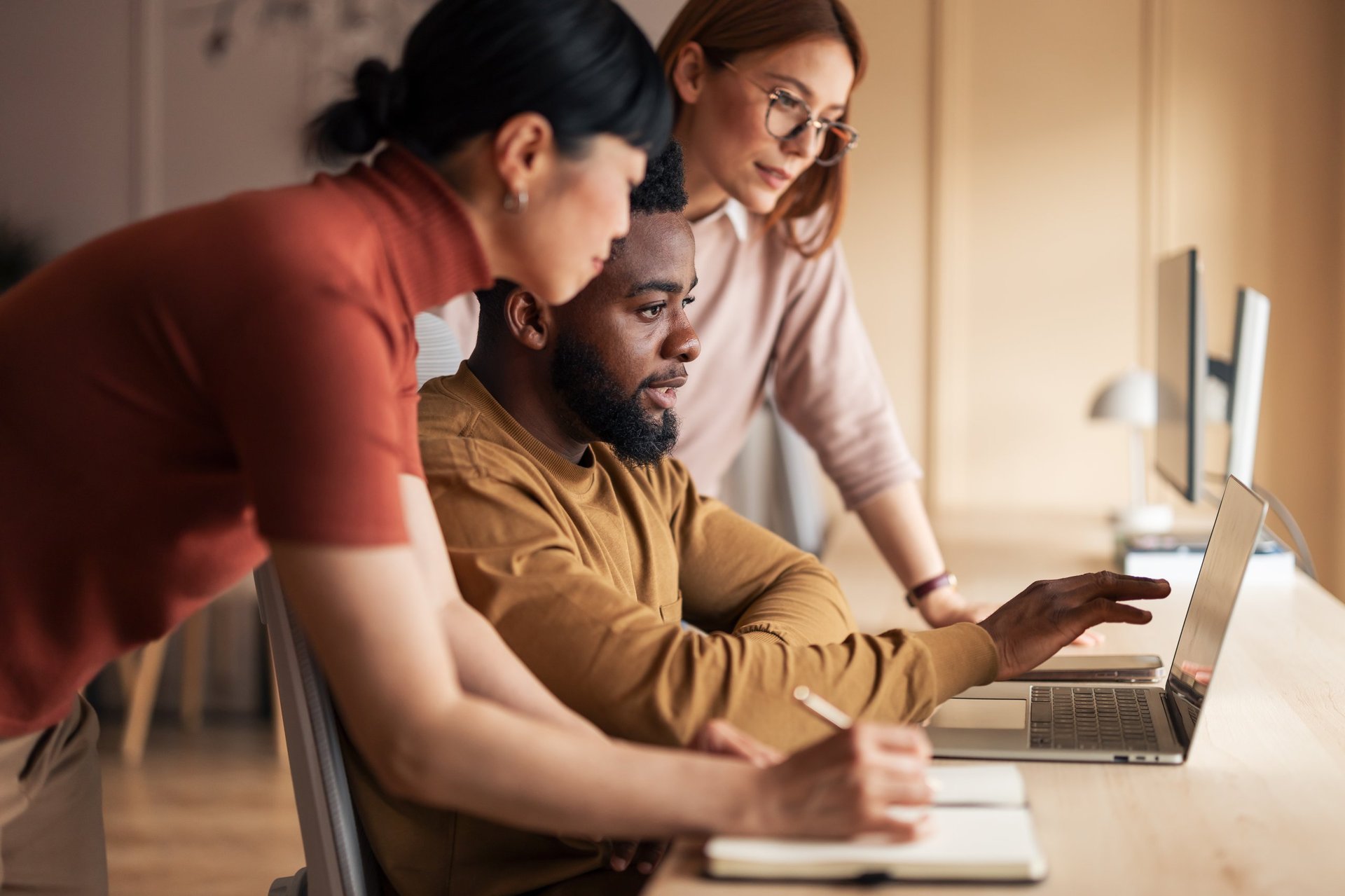 A team of professionals working collaboratively at a desk, using a laptop for a shared project in a modern office