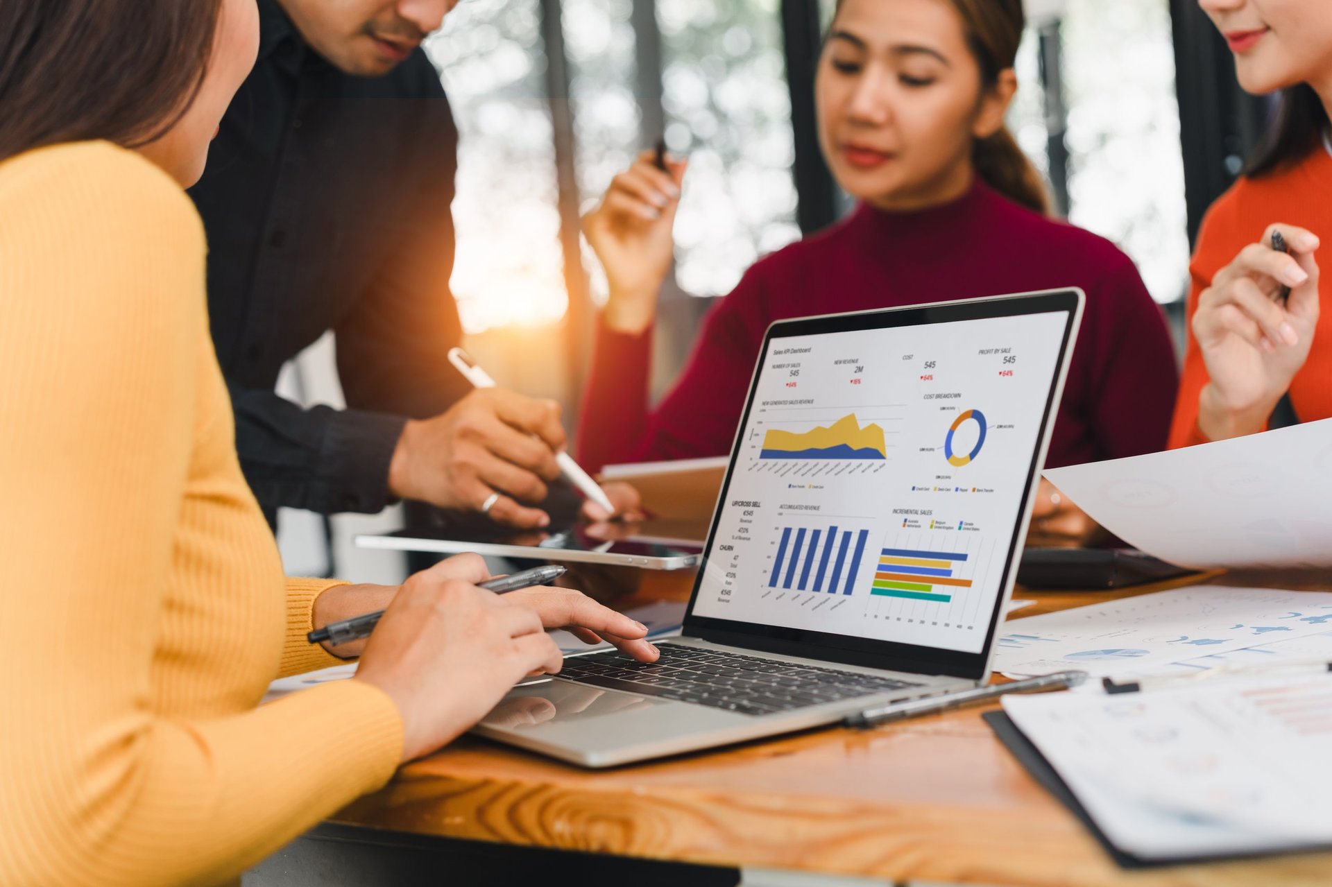A business team working on a data analysis project with a laptop showing charts and graphs, discussing strategy in a modern office
