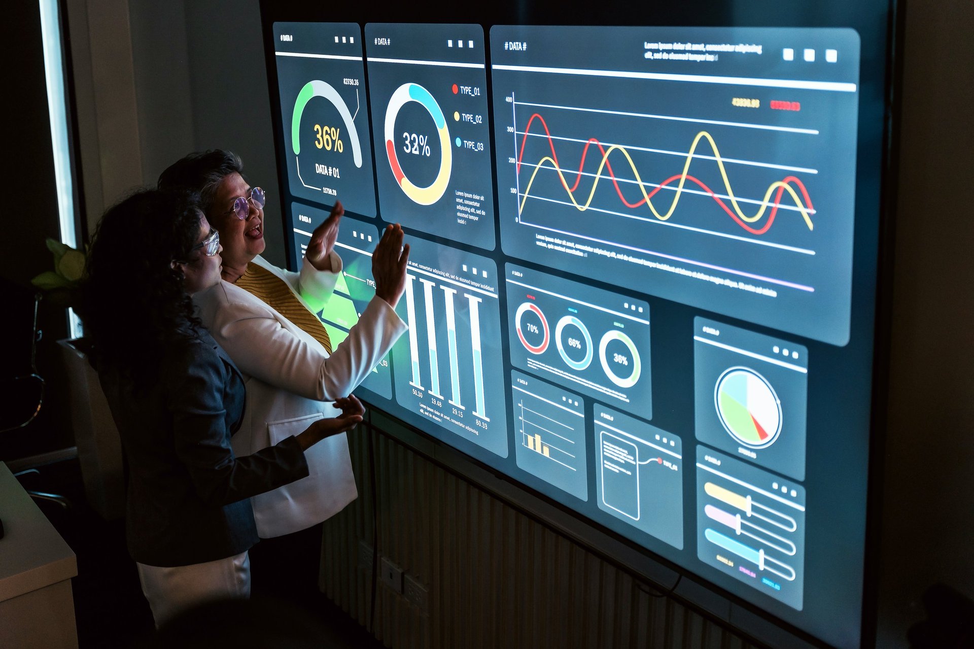 Two colleagues reviewing interactive charts on a large digital screen in a modern office, showcasing data-driven strategy