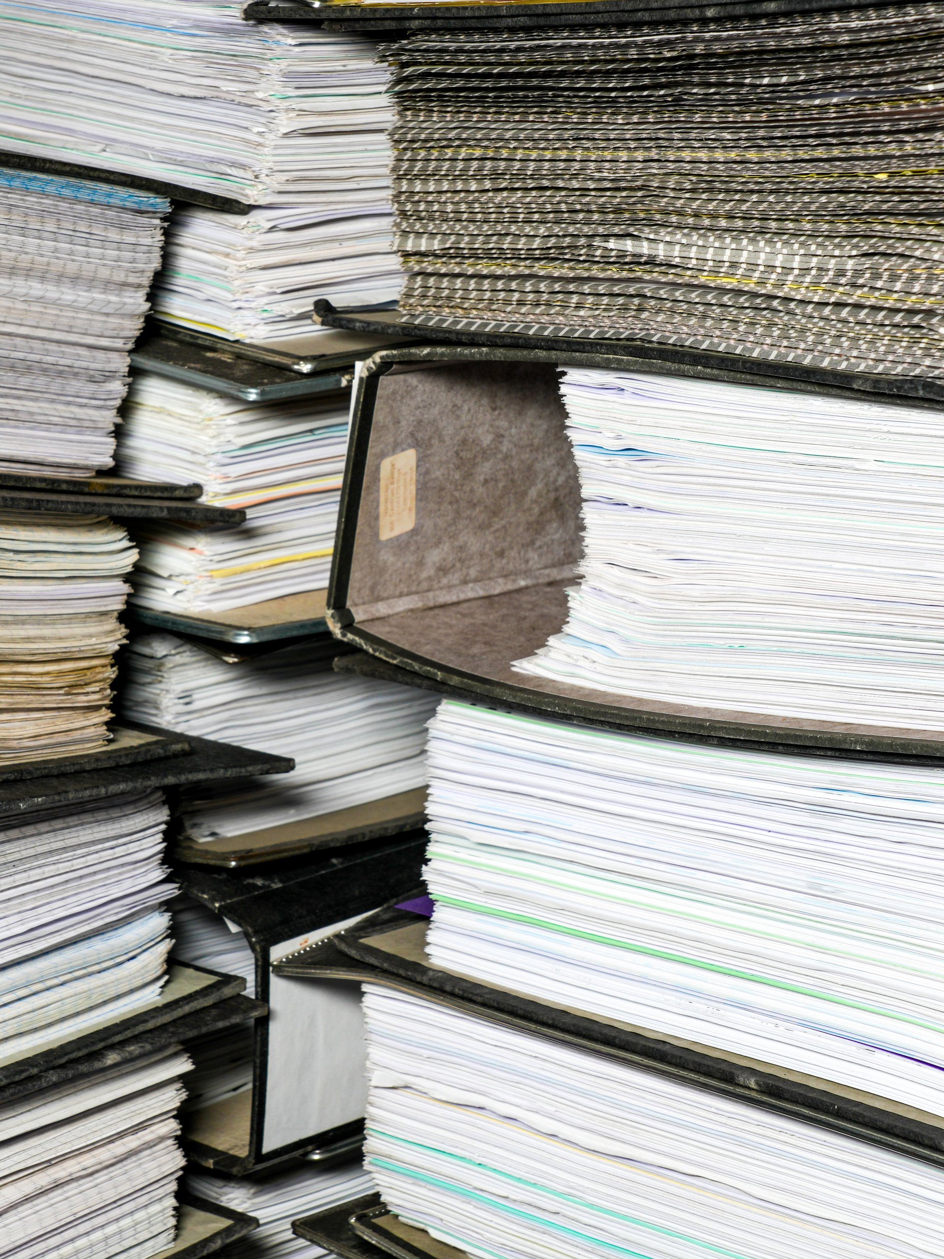 Stacks of paper document folders and manual records illustrating repetitive administrative work and duplicate data entry
