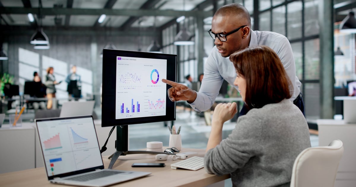 Two analysts reviewing workforce skills analytics and business performance metrics on laptops