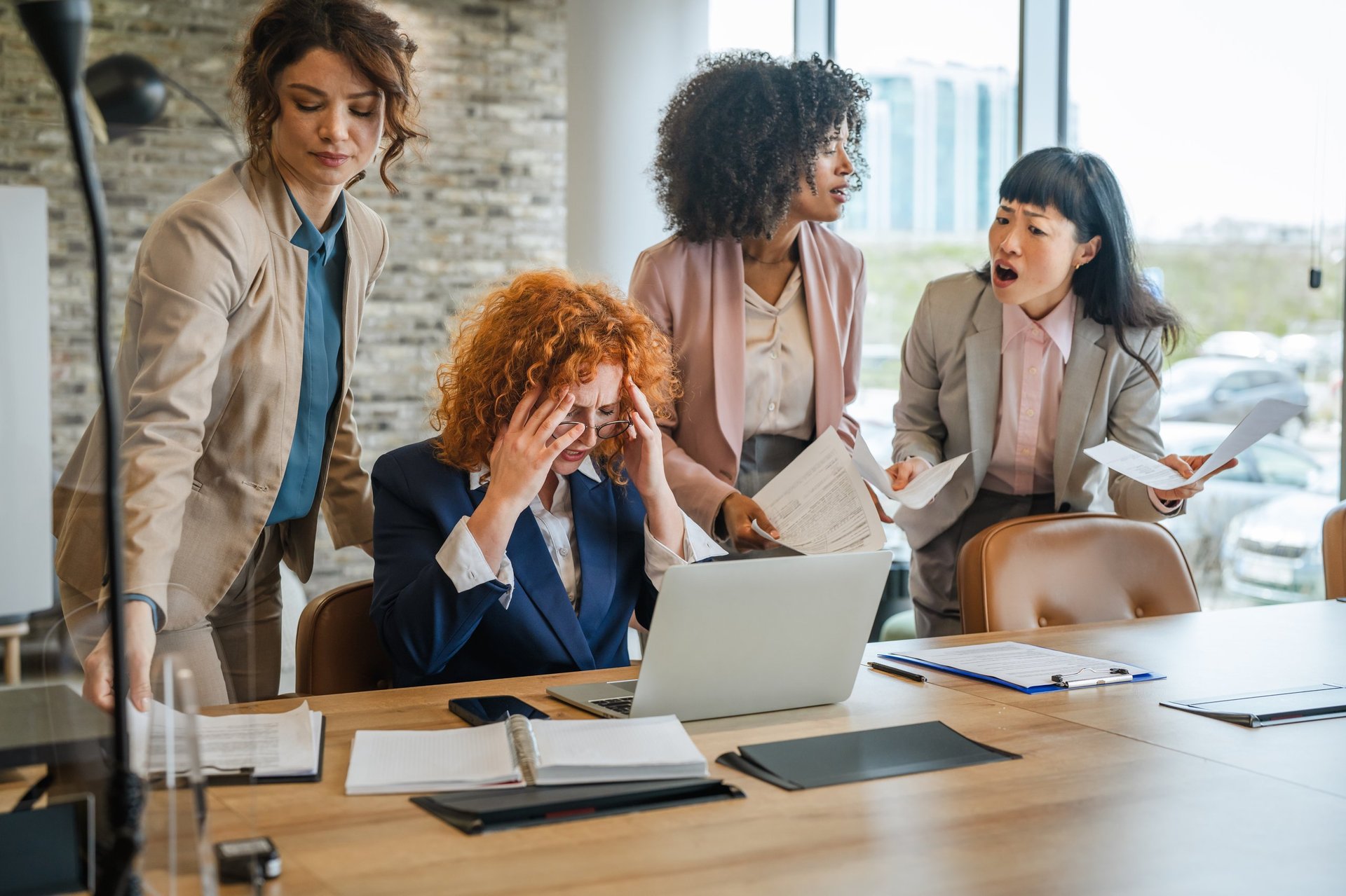 Businesswoman experiencing severe headache and burnout, surrounded by colleagues presenting more documents during an office meeting