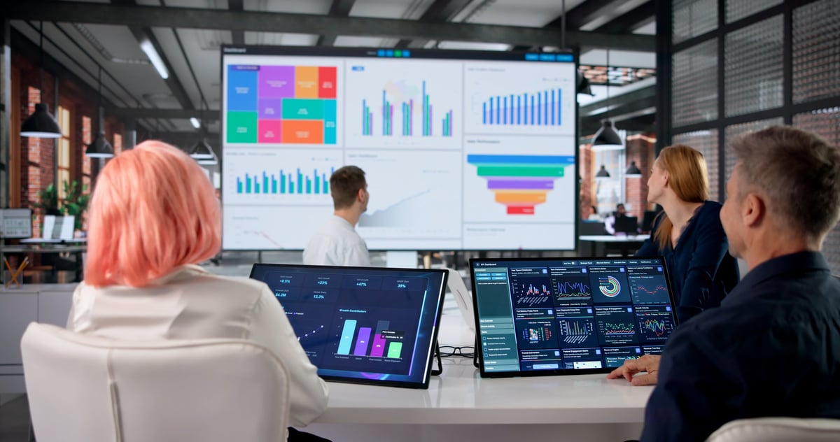 A financial analyst and team reviewing a colourful data dashboard during a meeting, representing ERP and analytics transformation work