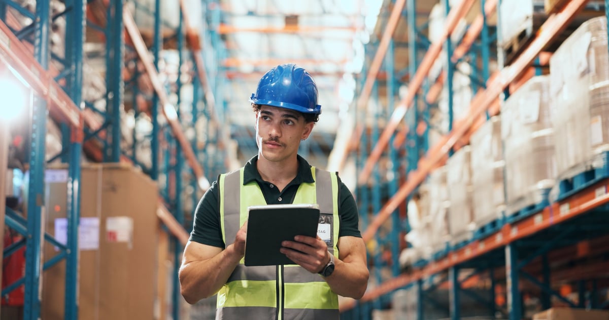 A worker in a warehouse using a tablet for stock quality control and order distribution, representing supply chain and logistics operations