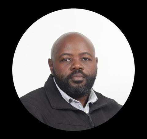 Professional headshot of a Black man with a beard, wearing a black jacket over a light blue shirt, against a white circular background