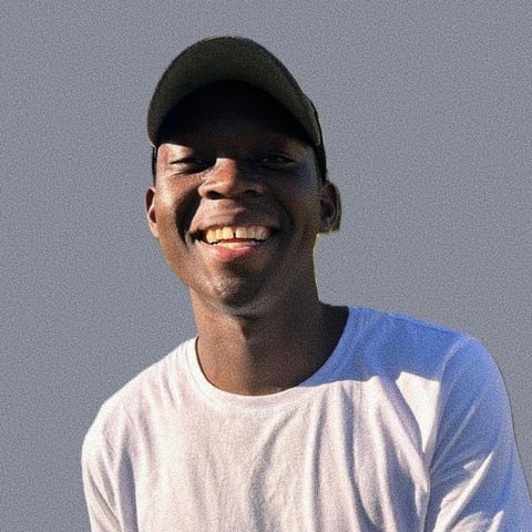 Portrait of a smiling man wearing a black baseball cap, blue and white shirt against gray background