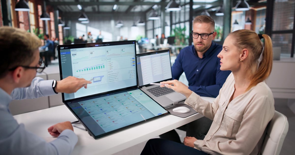 Four business professionals analyzing data on laptops and tablets at a modern office workspace.