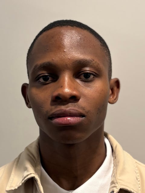 Headshot of a man with short dark hair wearing a beige or cream-colored shirt against a neutral beige background