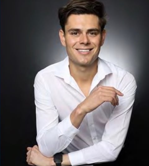 Smiling man in white button-up shirt posing for professional headshot against dark background