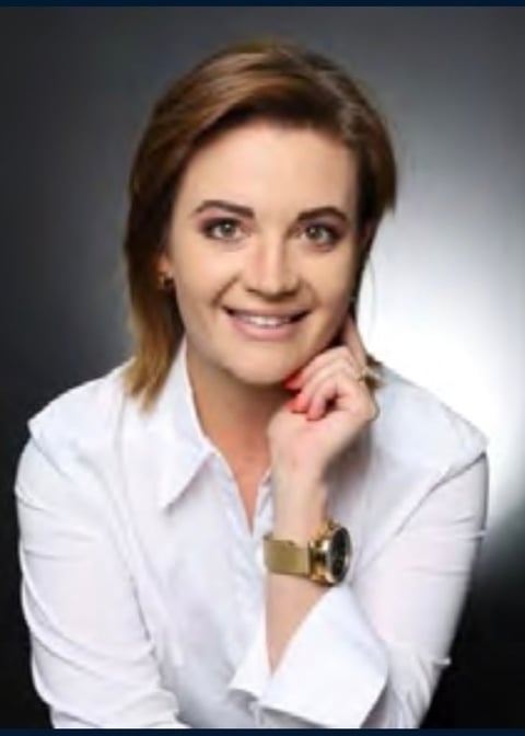 Professional headshot of a smiling woman with shoulder-length brown hair wearing a white button-up shirt and gold watch
