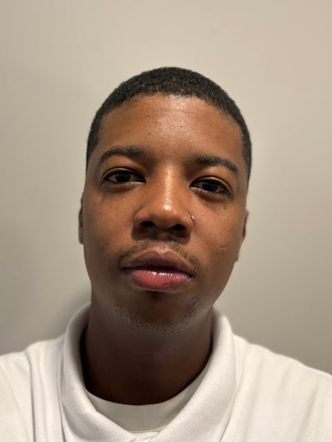 Portrait headshot of a man with short dark hair wearing a white t-shirt against a plain beige background