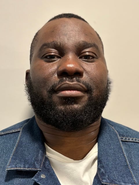 Portrait of a man with a beard wearing a denim jacket over a white shirt against a neutral background